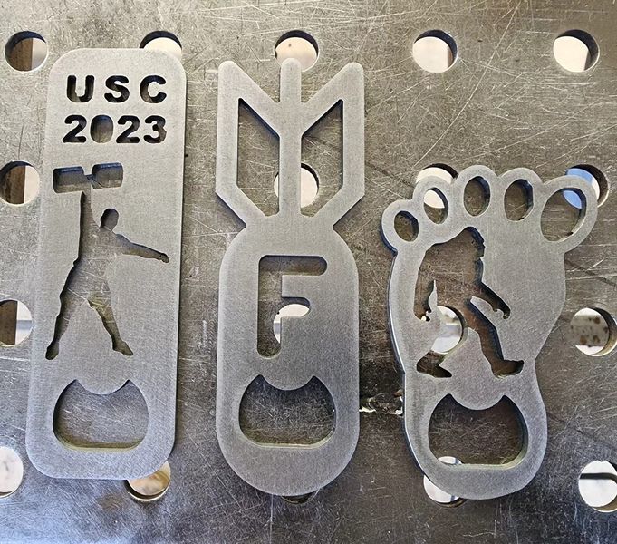 Three unique beer bottle openers are displayed on a metal surface.