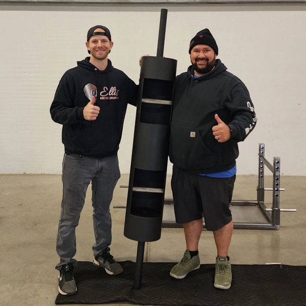 Two men pose with a newly crafted black weightlifting accessory, displaying thumbs up.